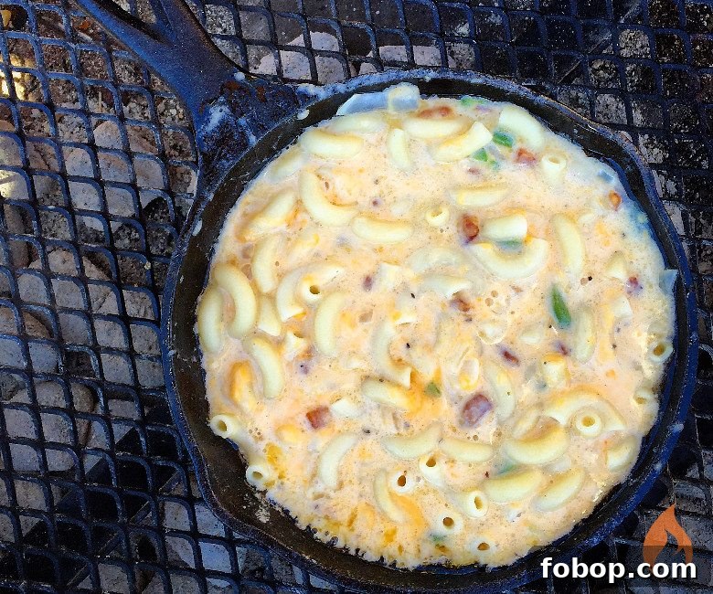 cast iron skillet of macaroni and cheese over a campfire