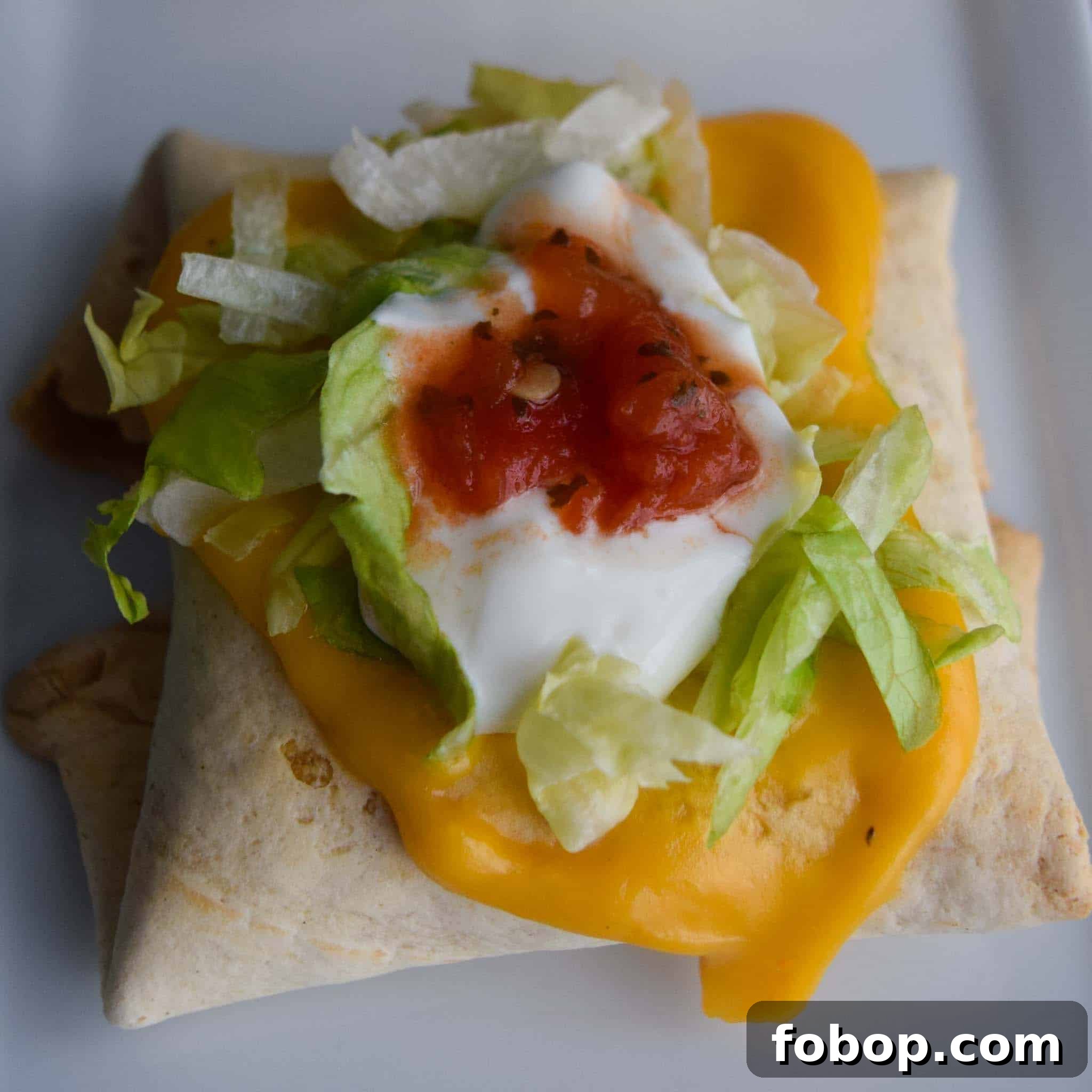 Baked Chimichangas with Guilt-Free Cheesy Sauce topped with lettuce sour cream and salsa close up view