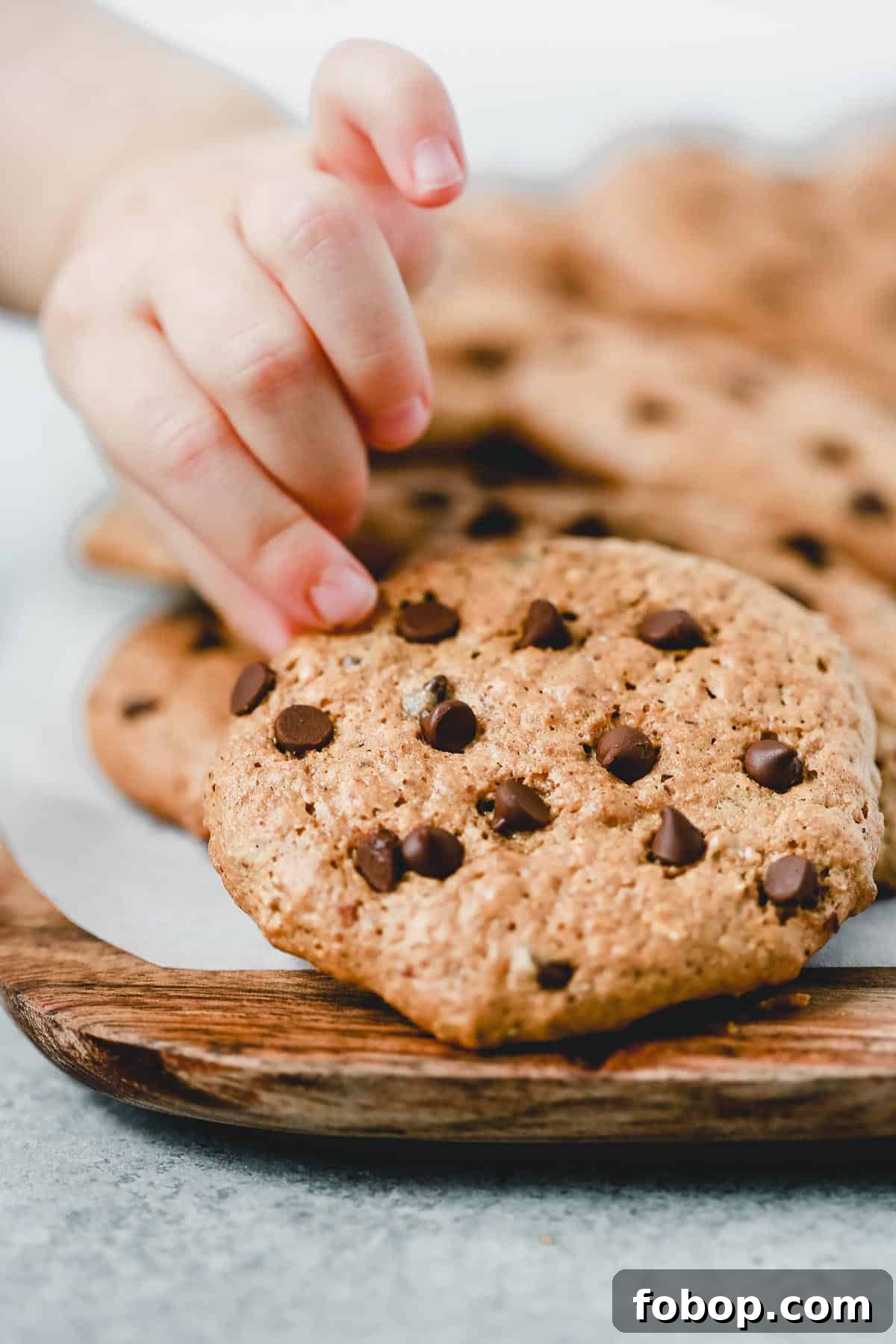 child's fingers pulling an almond butter chocolate chip cookie from a tray