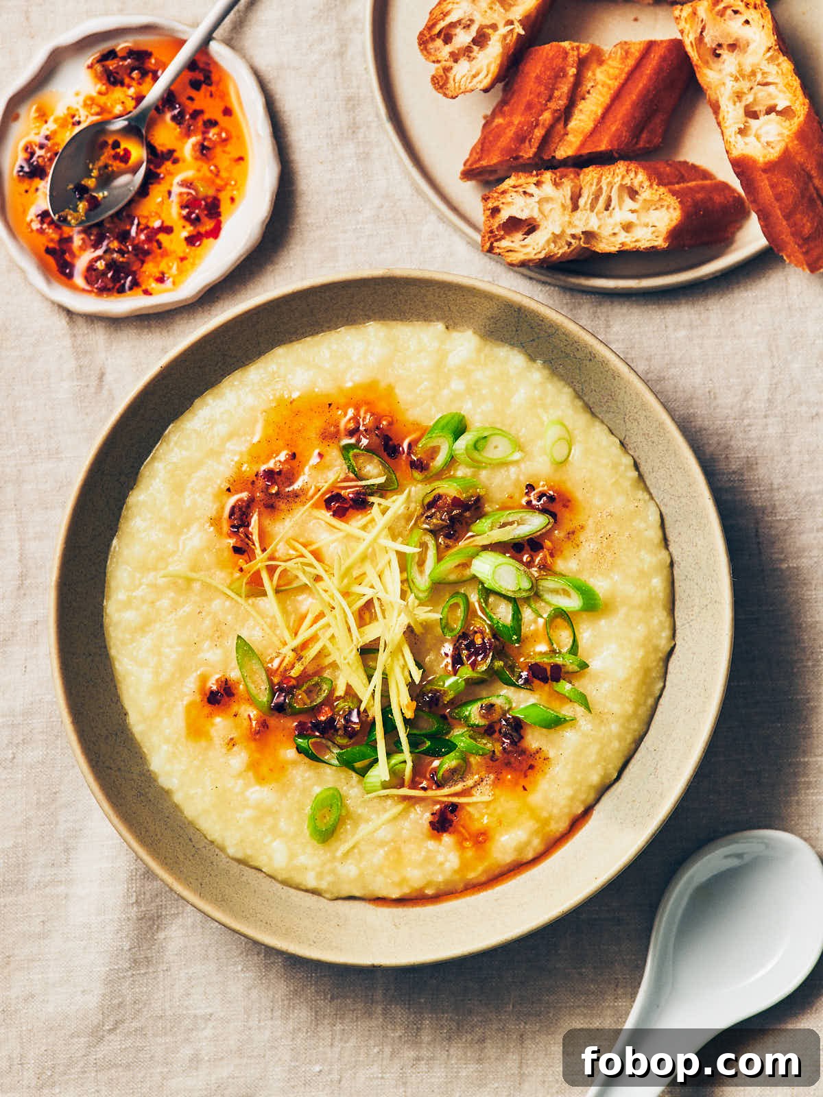 A bowl of vegan congee (rice porridge) topped with chili garlic oil, ginger, and scallions sitting on a table, next to a small plate of Chinese doughnut (Youtiao).