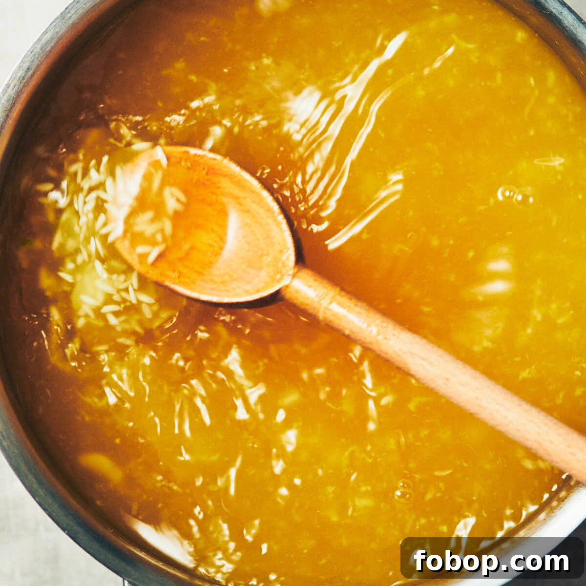 A spoon stirring vegetable stock, ginger, and garlic, into a pot of rice for congee.