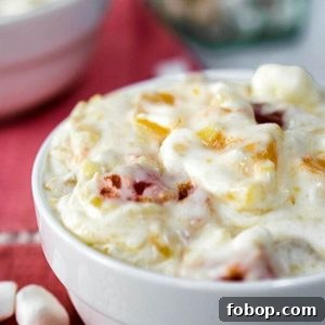 A whipped cream salad filled with fruit cocktail and cherries in a white bowl on top of a pink napkin.